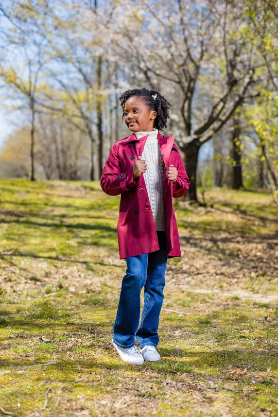 A joyful child wearing a rich berry trench coat outdoors, perfect for fall style and functionality.