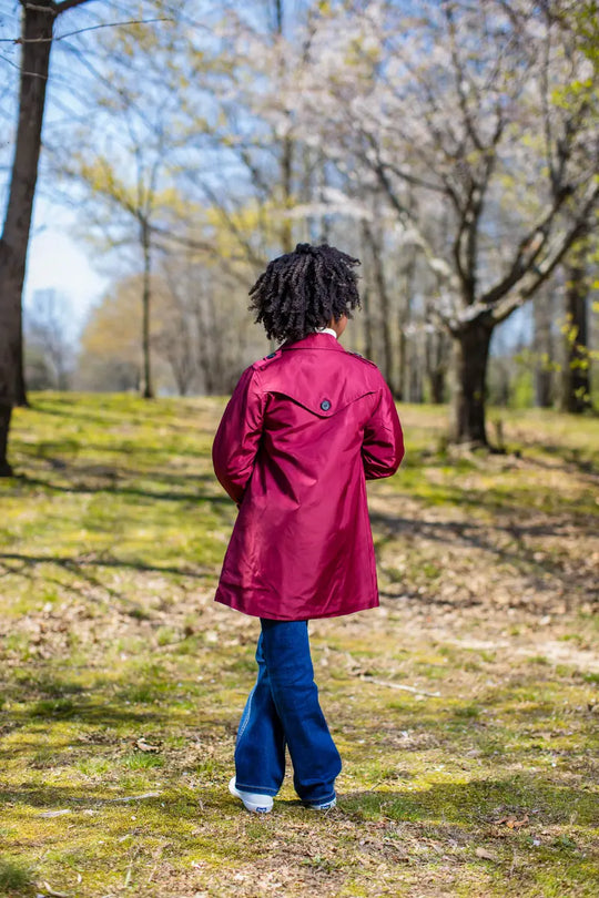 Back view of a person wearing a rich berry trench coat in a wooded area, showcasing style and comfort.