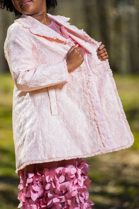 A young model showcasing a light pink embroidered coat, displaying its elegant lace design.