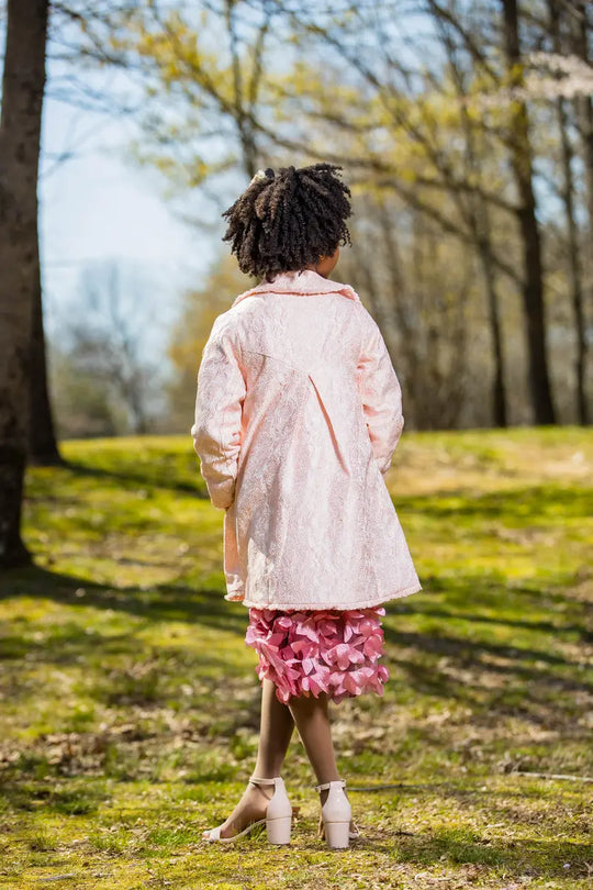 Girl wearing a light pink embroidered coat in a spring setting, showcasing floral details and a stylish look.