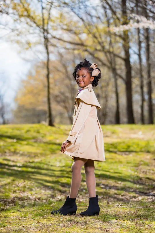 A young girl wearing a stylish checkered ribbon trench coat, smiling in a sunny outdoor setting.