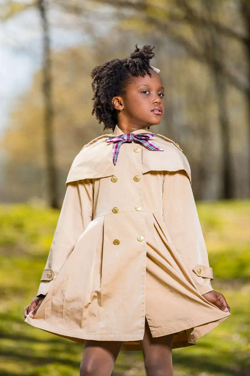 checkered ribbon trench coat displayed on a child standing in a park with autumn foliage in the background.