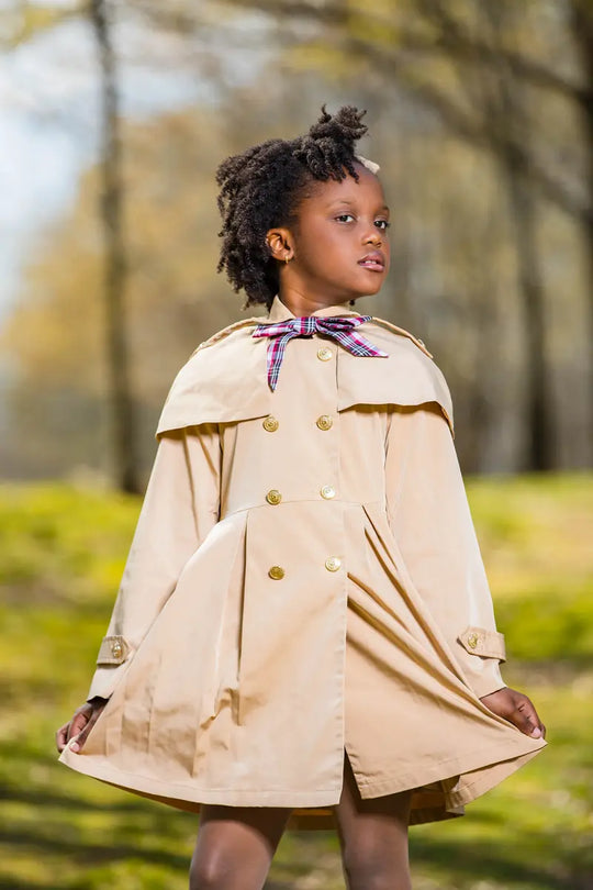 checkered ribbon trench coat displayed on a child standing in a park with autumn foliage in the background.