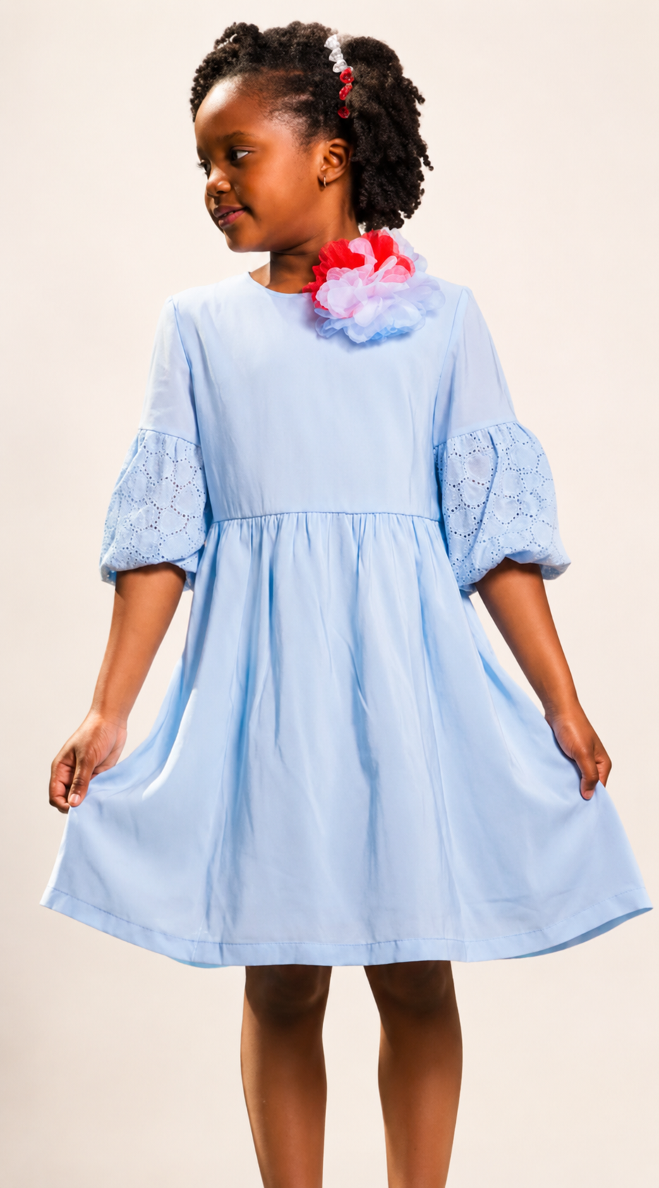 A young girl wearing an elegant light blue a-line dress with puffed sleeves and a colorful flower accessory.
